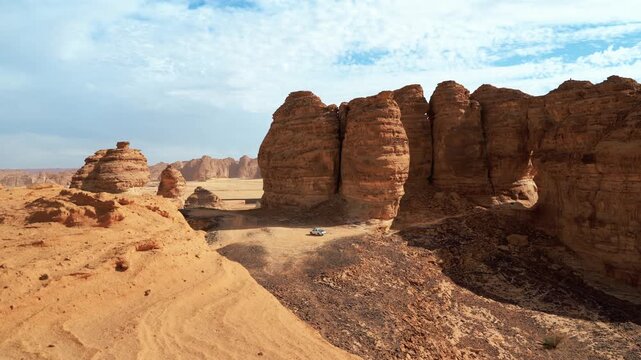 Sun shines to rocky desert landscape near Al Ula, view around from higher sandstone formation viewpoint near Vessel Hole Rock, small 4wd car in distance