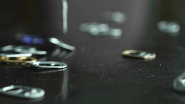 Pouring many colorful aluminum can tabs onto dark wooden table surface with sound
