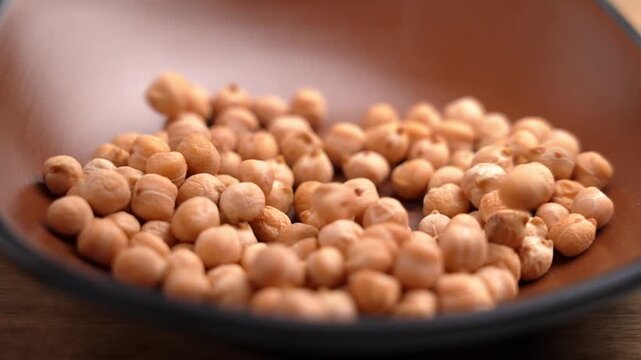 Organic garbanzo beans falling into a brown bowl in slow motion. Raw culinary ingredient. Uncooked legumes