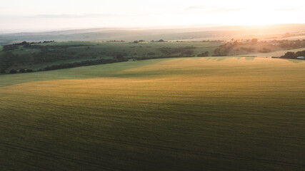 Naklejka premium Golden hour illuminates vast agricultural fields and rolling hills at sunrise