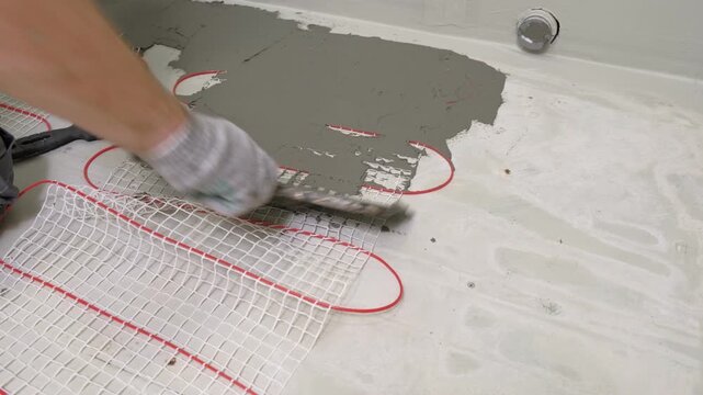 Construction worker preparing tile surface, mixing mortar substrate for flooring, underfloor heating mat. Workman combines adhesive in renovation setting. Operating power tool during bathroom upgrade