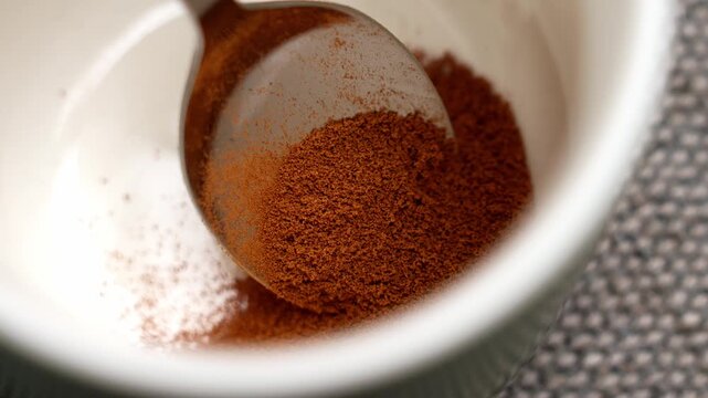 Spoon with granulated chicory powder falling into an empty ceramic mug in close up. Dry instant drink ingredient of caffeine free beverage