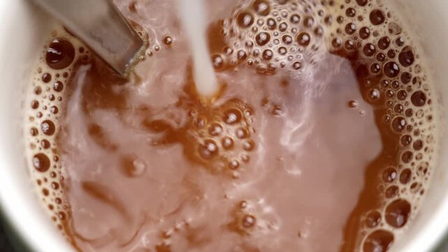 Milk pouring into a hot chicory drink creating creamy swirls and foam on the surface. Blending of light and dark tones in a ceramic cup. Slow motion