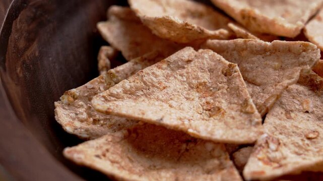 Crispy organic buckwheat tortilla chips served in a dark rustic wooden bowl. Gluten-free nachos with grains of amaranth and quinoa. Rotation