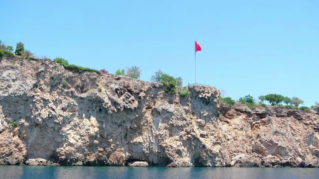Turkiye, Belek, 27.07.2025 Turkish flag waving on a high coastal cliff over the blue sea. Mountain landscape in Turkey for summer vacation. Mediterranean travel destination scenery clip.