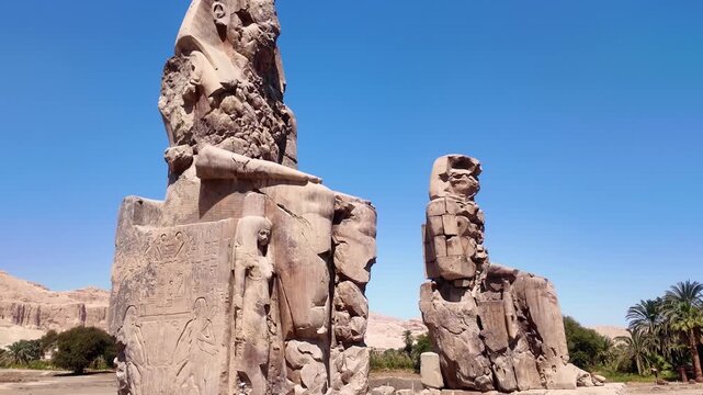 : Horizontal zoom out shot revealing the full scale of the Colossi of Memnon statues in Luxor, Egypt. Ancient Egypt and archaeology concept.