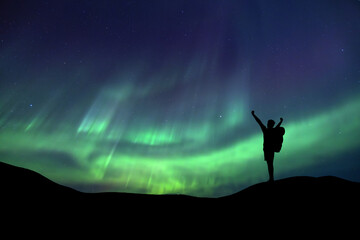 A person is observing a magnificent Aurora Borealis light display in an open field Success concept. © Philip
