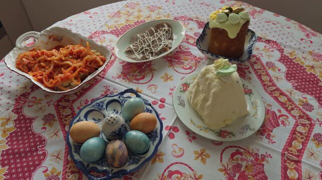 Easter celebration featuring ornate dishes and vibrant decor scene. Decorative Easter eggs complemented by paskha dessert and fresh vegetable salads on floral tablecloth in cozy home setting
