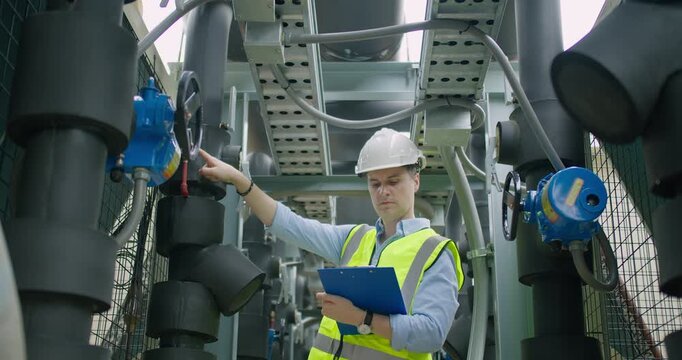 An industrial engineer performs a maintenance inspection on a building's HVAC system, pointing at a pressure valve to ensure safety and operational efficiency.