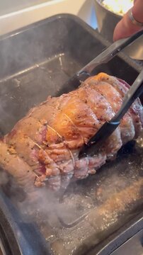 Vertical video social media - Closeup of a hand using a pair of tongs to turn a raw topside joint of beef, searing in juices, inside a smoking hot oven baking tray, before the main oven cooking.