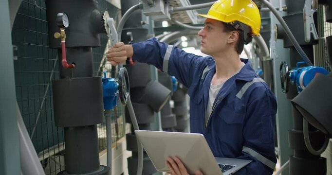 A male technician in a hard hat inspects an HVAC system with a laptop, performing quality control and maintenance checks in an industrial plant.