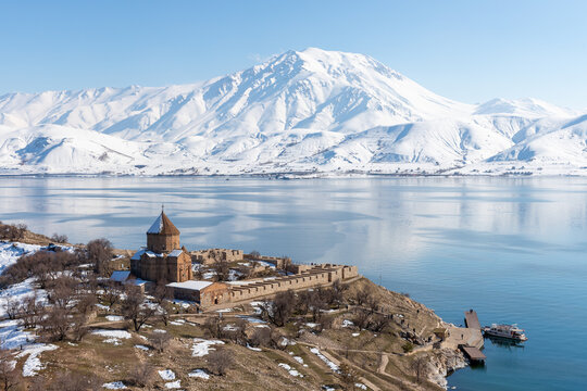 View of Akdamar Island with Holy Cross Church, Lake Van and snow-covered mountains, highlighting cultural heritage and winter landscape in eastern T&uuml;rkiye