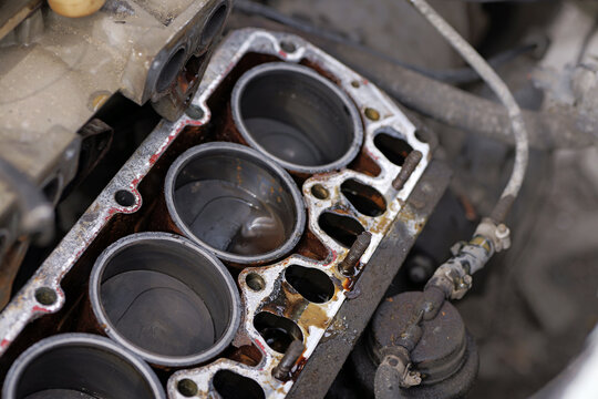 Four-cylinder engine block with removed cylinder head showing pistons, fluid contamination, and gasket residue, indicating maintenance and repair.