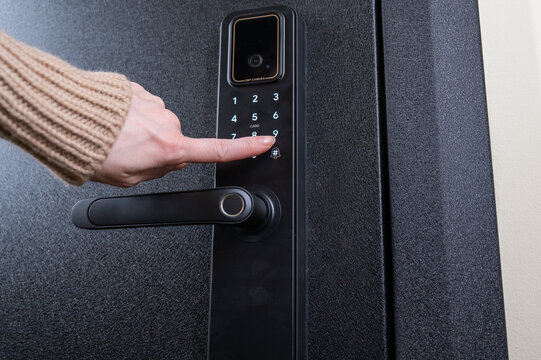 A woman opens a modern smart door lock with a digital keypad using a code.