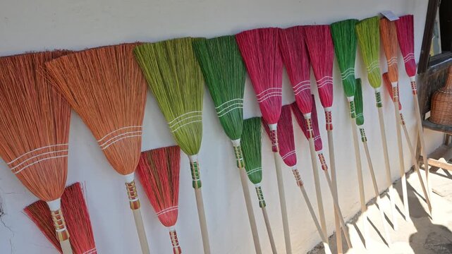 Handmade colorful traditional sorghum brooms leaning against a white wall.