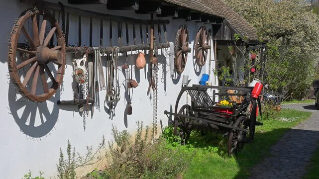 Traditional Hungarian farm tools and wooden wheels on house wall.