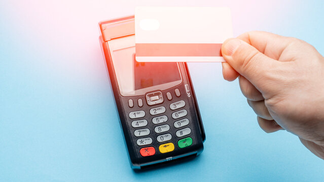 Hand inserts credit card into payment terminal. Terminal has keypad and screen. Bright light highlights payment action. Blue background adds modern feel. Shows modern payment process