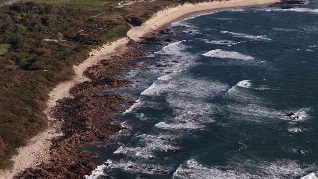 Aerial view of the rugged coastline where the deep blue sea crashes against the rocky shore, Vila Praia de Ancora, Portugal.