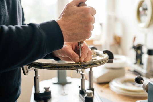 Technician pulling string through tennis racket frame using an awl on a machine