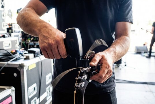Guitar technician using a string winder tool to change strings on an electric guitar