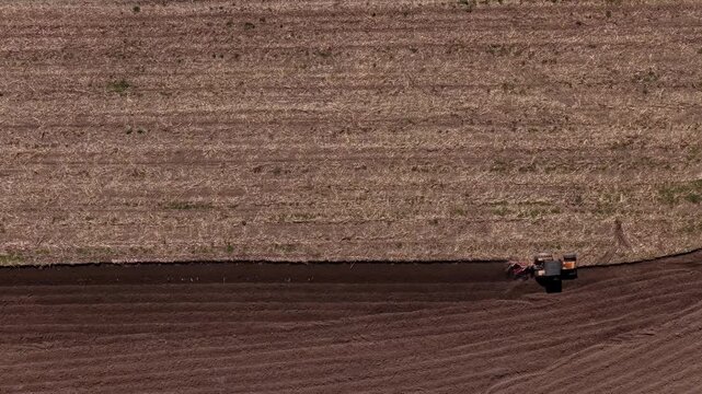 Aerial view of a tractor tilling the soil, creating a stark contrast between the dark, freshly turned earth and the light brown of the uncultivated field, Ponte de Lima, Portugal.