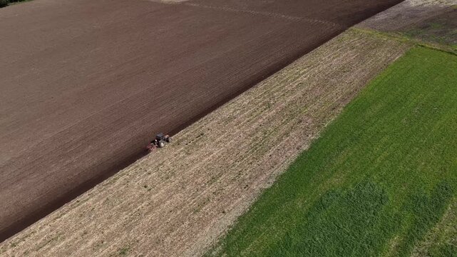 Aerial view of a tractor tilling soil in brown and green patchwork fields, creating a textured pattern in the landscape, Ponte de Lima, Portugal.