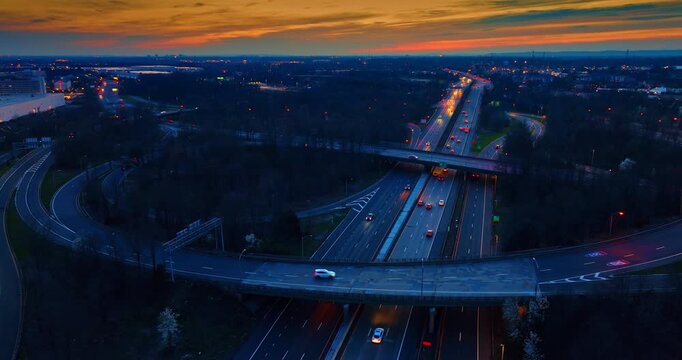 Cars with headlights on go by the highways and trestles. Moving over the large intersection at dusk time.