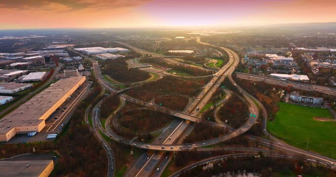 Huge interchange crossing the cityscape dazzled by the setting sun. Lively intersection in the suburbs. Aerial view.