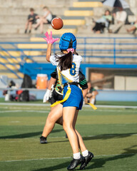 Fototapeta premium Female flag football receiver leaps for a high pass while closely defended during a competitive outdoor game.
