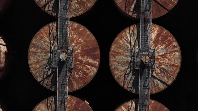 Aerial view of industrial site with rusty circular tanks connected by walkways, creating a geometric pattern of rust and shadow, Vila Real, Portugal.