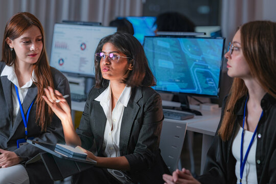 Confident Indian female AI security expert leading a discussion with colleagues in a dark SOC. Multiethnic women collaborating on threat intelligence and machine learning defense at night.