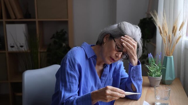 Unwell senior woman feeling sick measuring high temperature with thermometer