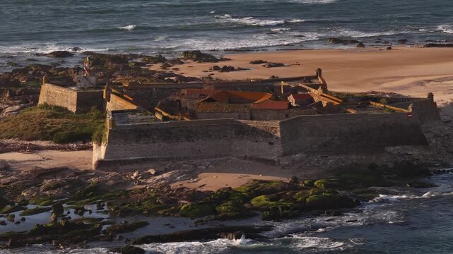Aerial view of Forte de Insua, a stone fortress on a small island, surrounded by the ocean with a beach nearby, Moledo, Portugal.
