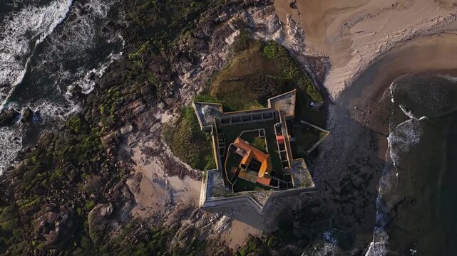 Aerial view of Forte de Insua, a star-shaped fortress standing firm against crashing waves and sandy beaches, Moledo, Portugal.