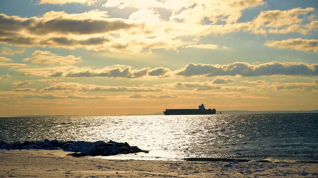 Bright sun lights the clouds and waterscape. Silhouette of the ship on the horizon.