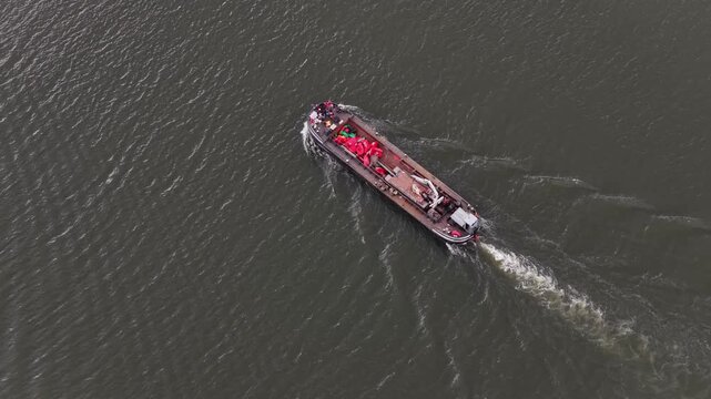 Aerial view of a lone boat cuts through the tranquil river surface, water trail visible, boat carrying red objects, Regua, Portugal.