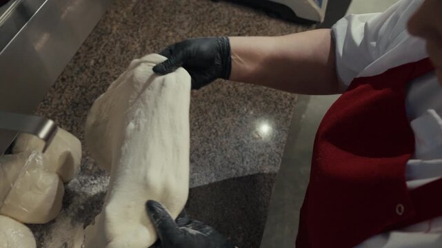 Caucasian male chef in red apron kneads and shapes pizza dough on a countertop, showcasing the process from ball to flat base in a commercial kitchen setting