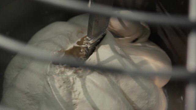 Dough being mixed in a commercial mixer, showing the continuous blending process with visible ingredients and mixing attachments in a professional kitchen setting