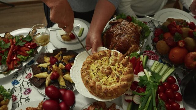 Hands of a Caucasian woman slicing a traditional bread dish on a festive table adorned with various colorful foods and drinks, creating a warm communal atmosphere