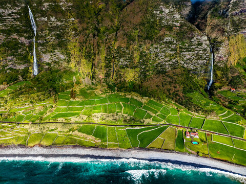Aerial view of cascading waterfalls meet the terraced fields and rugged coastline, contrasting with the turquoise waters of the Atlantic, Faja Grande, Azores, Portugal.