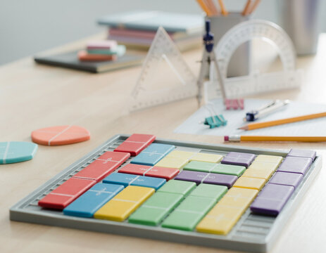A clear view of a math workshop table with brightly colored fraction tiles in focus, while geometry station materials are softly out of focus nearby.