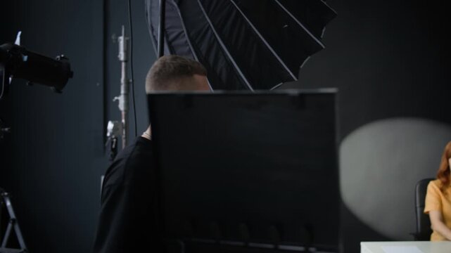 Tracking shot of young Caucasian man setting lightening in studio and starting recording woman who sitting at table