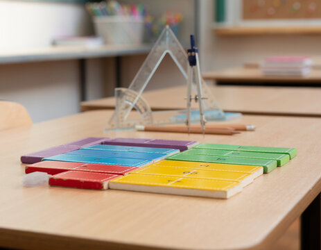 A clear view of a math workshop table with brightly colored fraction tiles in focus, while geometry station materials are softly out of focus nearby.