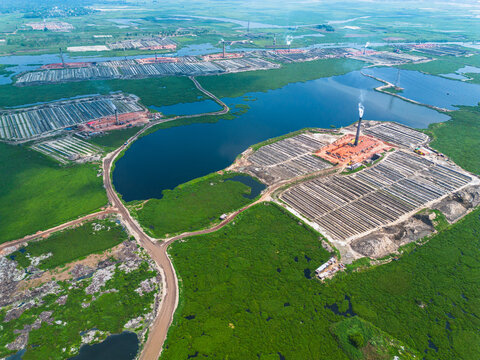Aerial view of industrial brick kilns rise amidst a verdant landscape, contrasting with the dark waters of the surrounding ponds, Dhaka, Dhaka Division, Bangladesh.
