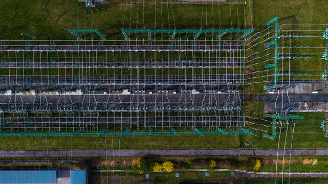Aerial view of a power station with intricate metal frameworks and crisscrossing cables amid green fields, Praha-Seberov, Hlavni mesto Praha, Czechia.