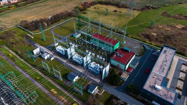 Aerial view of a power substation with vivid contrasts between the industrial metal structures, green vegetation, and red-roofed buildings, Praha-Seberov, Hlavni mesto Praha, Czechia.