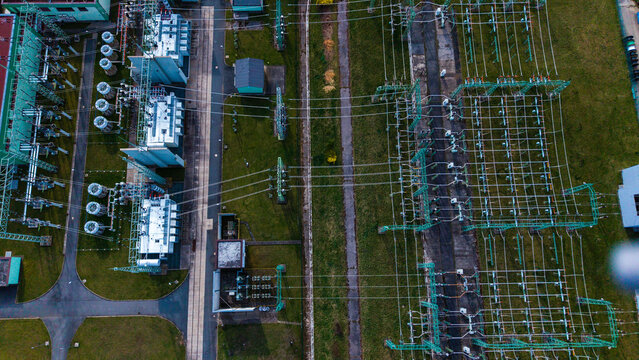 Aerial view of an electrical substation with high-voltage transformers and power lines contrasting against the green grass, Chodov, Hlavni mesto Praha, Czechia.
