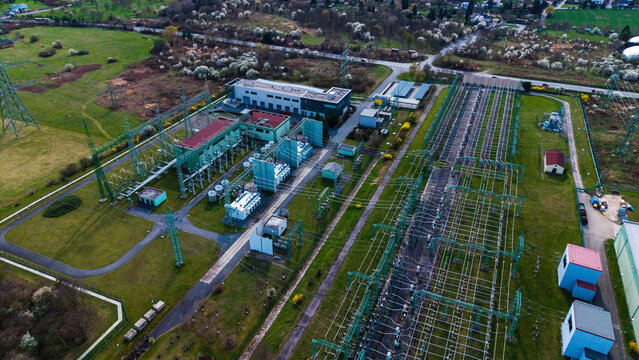 Aerial view of a modern electrical substation contrasts with the surrounding vibrant green fields and distant, muted trees, Praha-Seberov, Hlavni mesto Praha, Czechia.