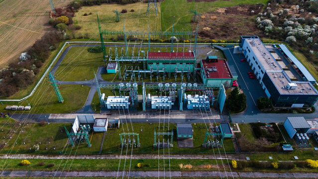 Aerial view of an electrical substation bathed in sunlight, its transformers and lines contrasting with the surrounding green fields, Praha-Seberov, Hlavni mesto Praha, Czechia.