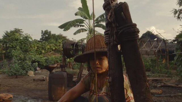 Female laborer pumping crude oil using a manual pump at an artisanal extraction site in Myanmar